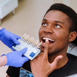 Man in dental chair pointing to teeth with dentist holding up shade guide