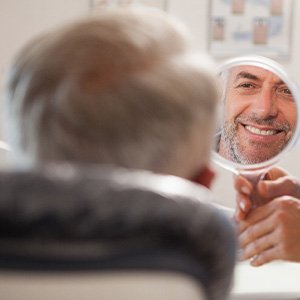 Man smiling at reflection in handheld mirror