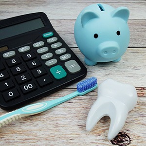 Blue piggy bank next to calculator, toothbrush, and model tooth on wooden surface