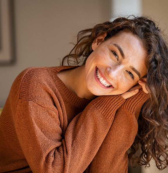Woman in brown sweater leaning on her hands smiling