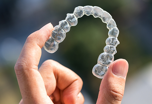 Close up of a hand holding a clear aligner