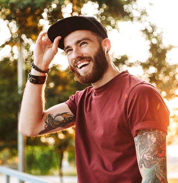 Young man with tattoo sleeves smiling outdoors after cosmetic dentistry in Rocky River