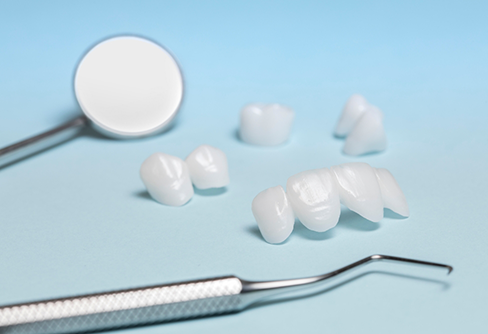 Several white dental crowns and veneers with dental mirror against light blue background