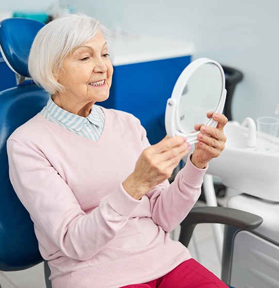 Happy senior dental patient smiling at herself in hand mirror