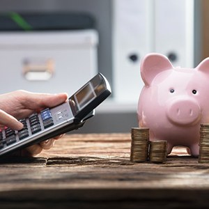 Someone operates pocket calculator near piggy bank
