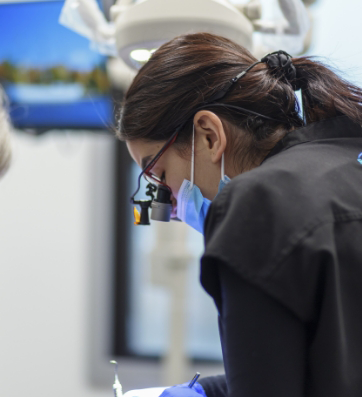 Dentist wearing face mask and dental binoculars while treating a patient