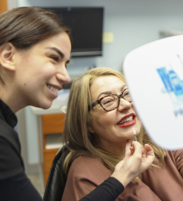 Woman in dental chair looking at her smile in a mirror