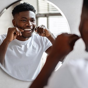 Man smiling while flossing his teeth in bathroom