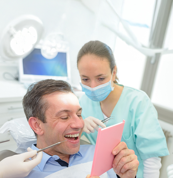 Man looking at his teeth in a mirror after restorative dentistry