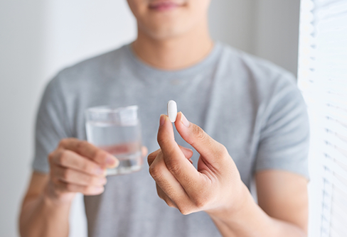 Person holding a glass of water and a white pill