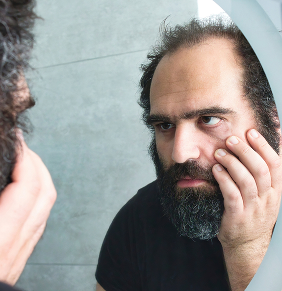 Frustrated man looking at his face in the mirror