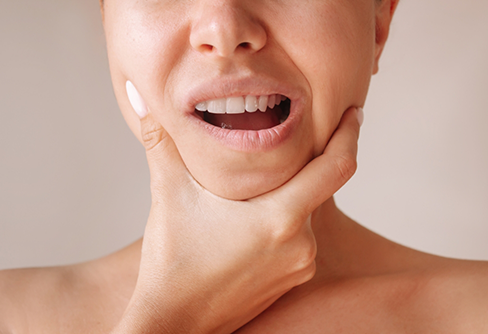 Person holding the sides of their jaw in pain before T M J treatment