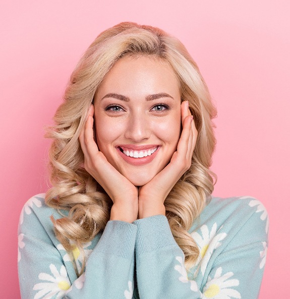 Woman smiling with hands touching her cheeks with pink background 