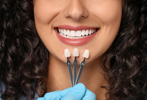 Nose-to-neck view of woman smiling with shade guide held up to teeth
