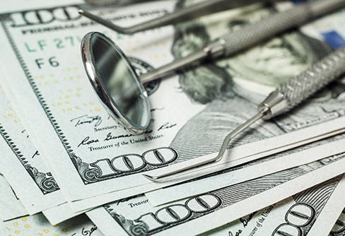 Several $100 bills under dental instruments