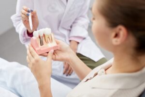 Dentist pointing to model of dental implant held by patient.